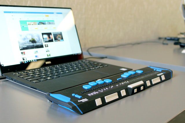 A Braille display attached to a black laptop on a grey desk