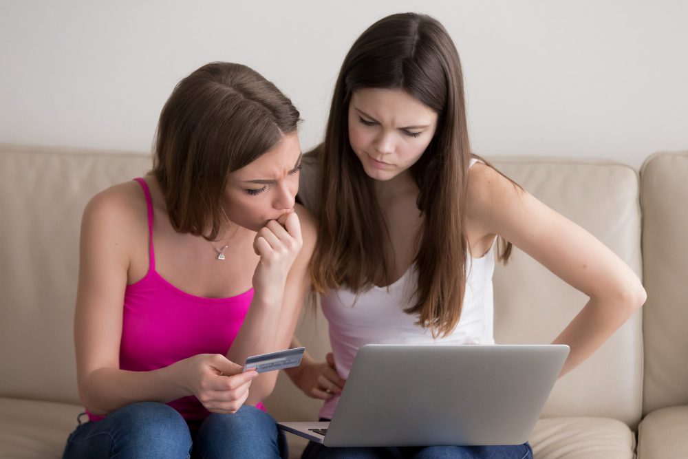 two women holding a laptop and a credit card