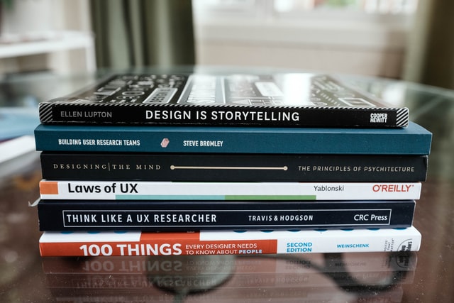A stack of UX design books sitting on a glass table
