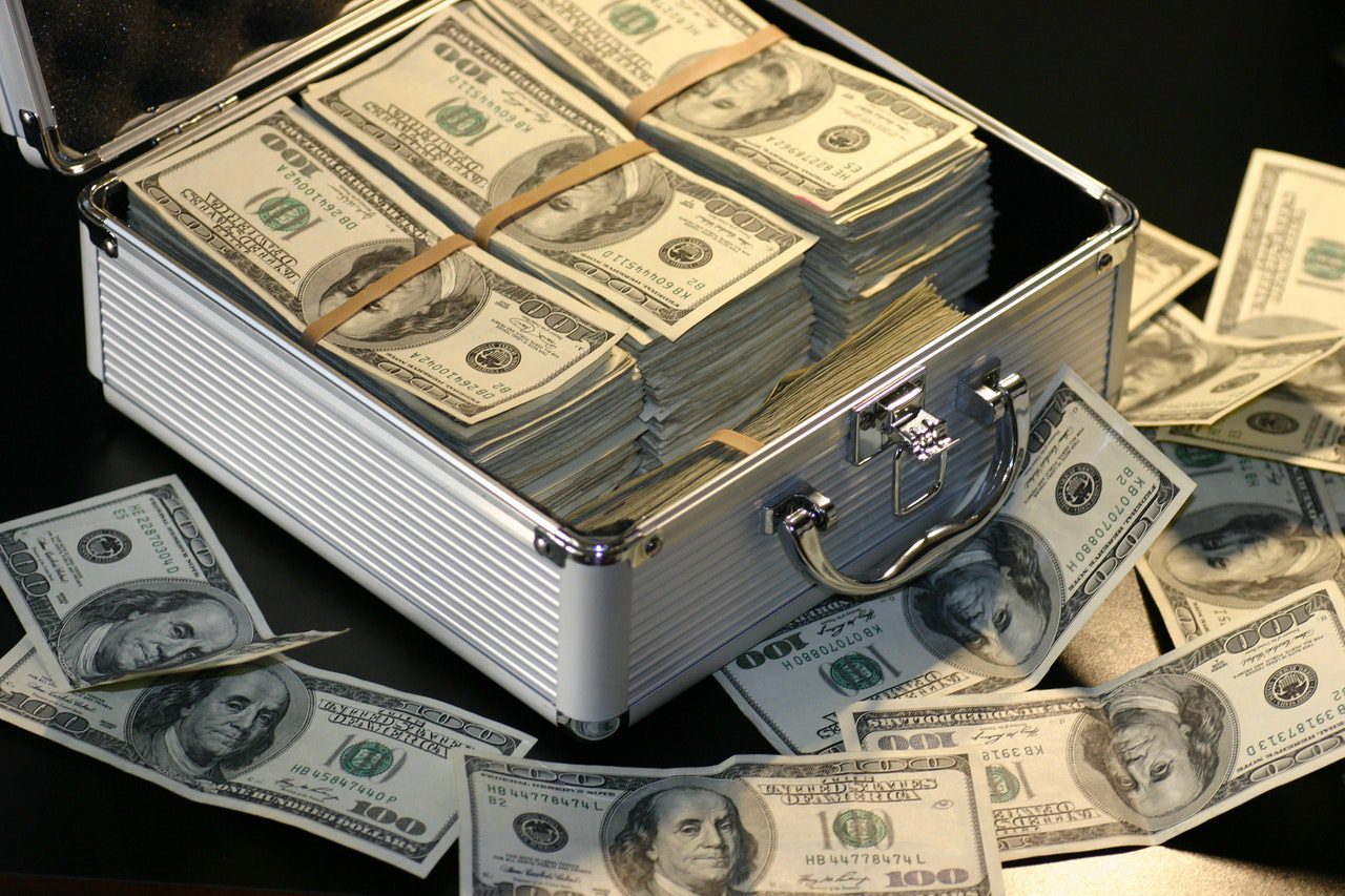piles of 100 dollar bills in a metal case surrounded by loose bills